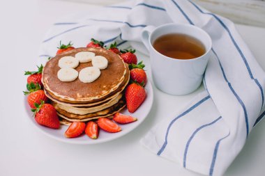 Sağlıklı kahvaltı. Krep çilek, muz, beyaz havlu ile beyaz arka planda siyah çay