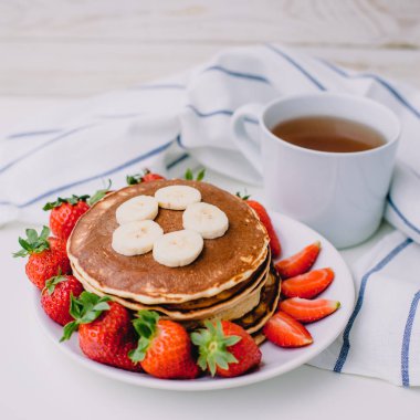 Sağlıklı kahvaltı. Krep çilek, muz, beyaz havlu ile beyaz arka planda siyah çay
