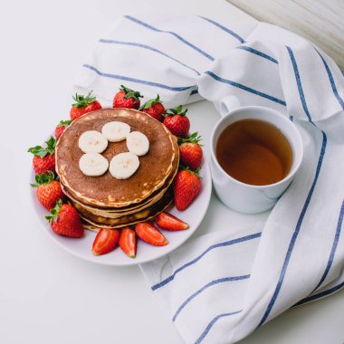 Sağlıklı kahvaltı. Krep çilek, muz, beyaz havlu ile beyaz arka planda siyah çay