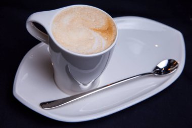 Latte bir restaurantında beyaz uzun plaka üzerinde beyaz Kupası'nda uzun latte kaşıkla besleme kahve fincan 