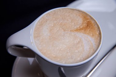 Latte bir restaurantında beyaz uzun plaka üzerinde beyaz Kupası'nda uzun latte kaşıkla besleme kahve fincan 