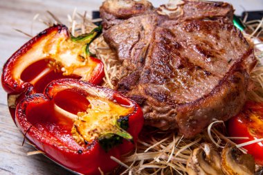 Domuz eti sığır eti biftek ızgara biber, domates ve Tabasco sos plaka saman şeklinde dekor ve biftek için bir bıçak ile ızgara, mantar ile