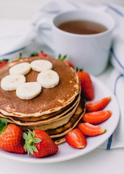 Zdrowe śniadanie. Naleśniki z truskawek, bananów, filiżankę herbaty czarnej na białym tle biały ręcznik — Zdjęcie stockowe