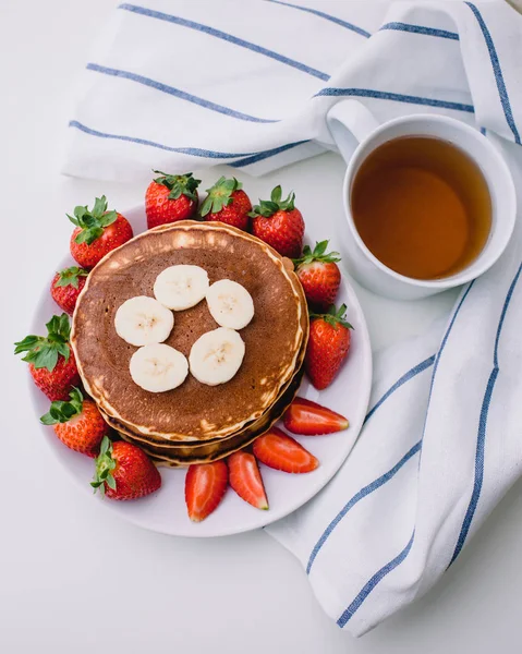Sağlıklı kahvaltı. Krep çilek, muz, beyaz havlu ile beyaz arka planda siyah çay