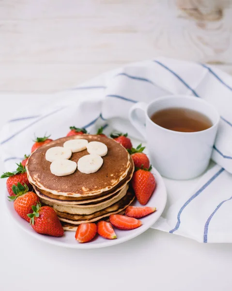 Sağlıklı kahvaltı. Krep çilek, muz, beyaz havlu ile beyaz arka planda siyah çay