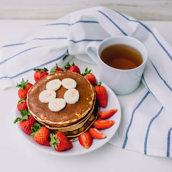 Sağlıklı kahvaltı. Krep çilek, muz, beyaz havlu ile beyaz arka planda siyah çay