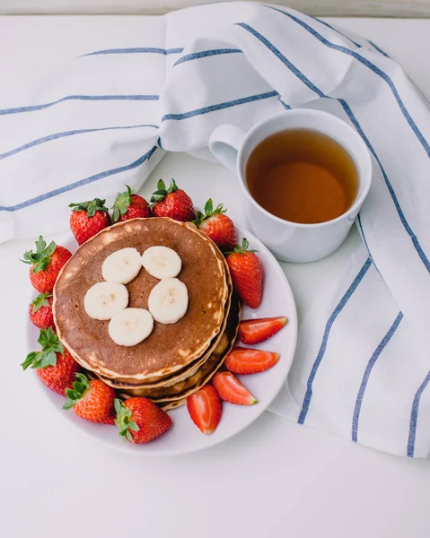 Sağlıklı kahvaltı. Krep çilek, muz, beyaz havlu ile beyaz arka planda siyah çay