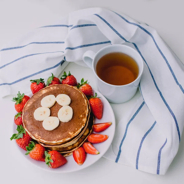 Sağlıklı kahvaltı. Krep çilek, muz, beyaz havlu ile beyaz arka planda siyah çay