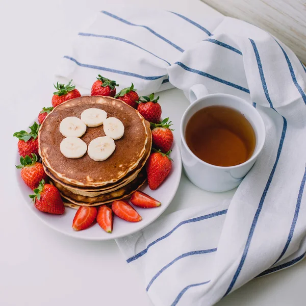 Sağlıklı kahvaltı. Krep çilek, muz, beyaz havlu ile beyaz arka planda siyah çay