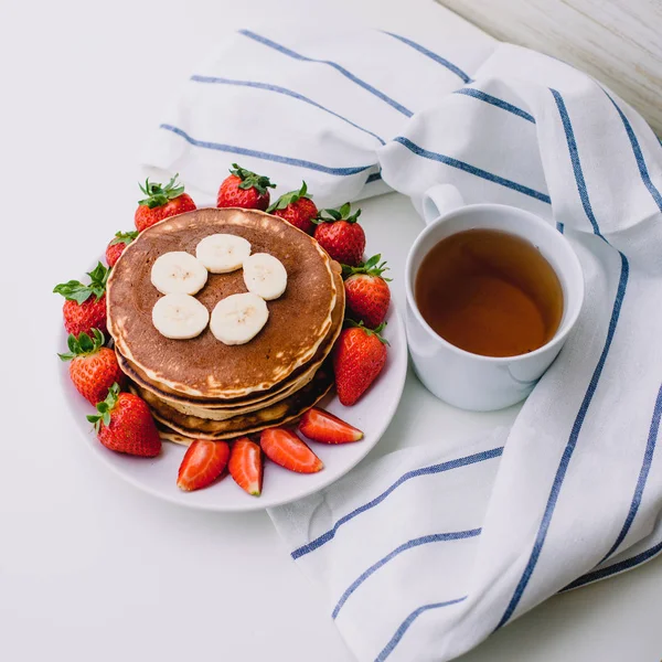 Sağlıklı kahvaltı. Krep çilek, muz, beyaz havlu ile beyaz arka planda siyah çay