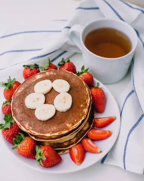 Sağlıklı kahvaltı. Krep çilek, muz, beyaz havlu ile beyaz arka planda siyah çay