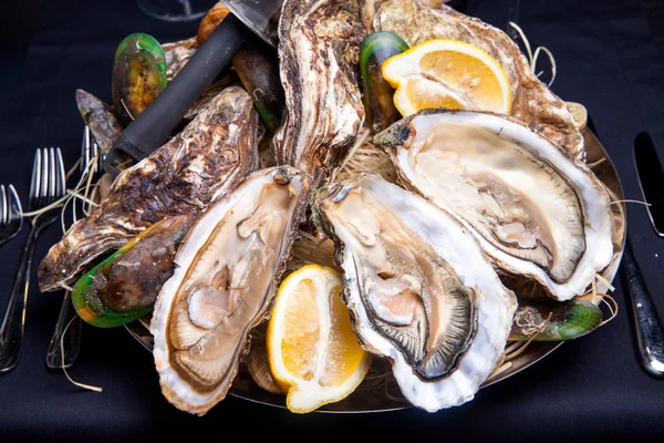 Öppnade ostron på Folkmusik inredda plattan med citron och oyster kniv i restaurang utfodring med ros champagne — Stockfoto