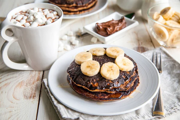 Breakfast for couple included oat pancakes with banana, nutella, honey, with coffe and milk and cacao with marshmallow on white wooden  background