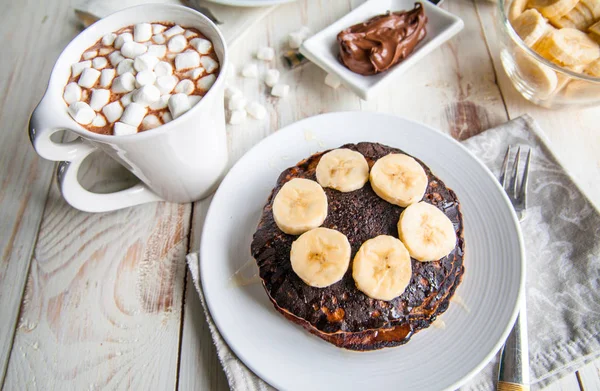 Breakfast for couple included oat pancakes with banana, nutella, honey, with coffe and milk and cacao with marshmallow on white wooden  background