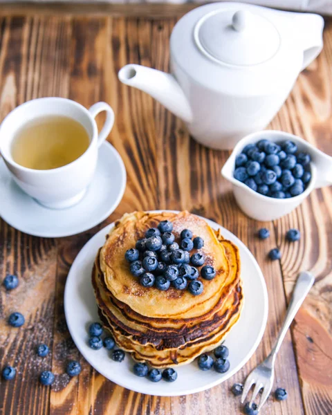 Egészséges reggeli, áfonya, áfonya láp csésze zöld tea, fekete áfonya és a teáskanna barna fa háttér csésze palacsinta — Stock Fotó