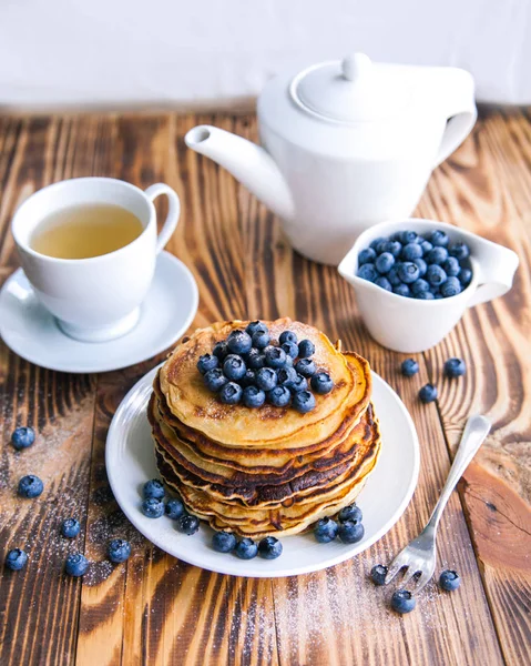 Egészséges reggeli, áfonya, áfonya láp csésze zöld tea, fekete áfonya és a teáskanna barna fa háttér csésze palacsinta — Stock Fotó
