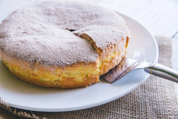 Biscuit de tort de mere de casă aproape de o felie de tort pe placă albă pe fundal alb din lemn — Fotografie, imagine de stoc