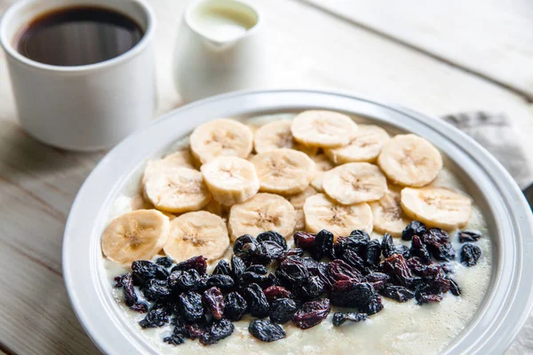 Fitness diet healthy Breakfast which included oatmeal oat porridge with milk, banana and  raisins without sugar and fat with cup of coffee with milk on the white wooden background