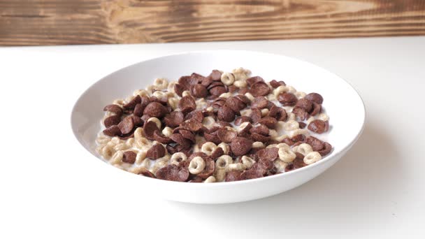 Ontbijt inbegrepen cornflakes, melk en frambozen. Frambozen vallen op een witte plaat met melk en cornflakes in slow motion. — Stockvideo