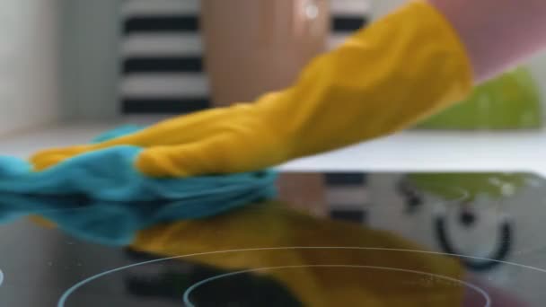 Жінка миє плиту. Руки в жовтих рукавичках миють індукційну плиту. Жінка прибирає будинок — стокове відео