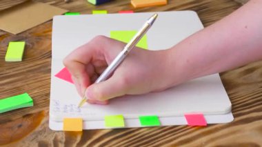 Kadın Notlar not defteri yazın. Ofis, banka donatımı ile açık not etmek. Marker, kalem, kalem ve çıkartmaları ile ahşap bir masaüstünde açık not defteri yatıyor