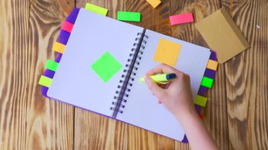 Kadın Not Defteri'ni açar ve gülümseme çizer. Ofis, banka donatımı ile açık not etmek. Marker, kalem, kalem ve çıkartmaları ile ahşap bir masaüstünde açık not defteri yatıyor