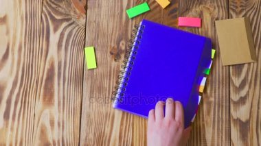 Kadın Not Defteri'ni açar ve gülümseme çizer. Ofis, banka donatımı ile açık not etmek. Marker, kalem, kalem ve çıkartmaları ile ahşap bir masaüstünde açık not defteri yatıyor
