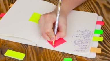 Kadın Notlar not defteri yazın. Ofis, banka donatımı ile açık not etmek. Marker, kalem, kalem ve çıkartmaları ile ahşap bir masaüstünde açık not defteri yatıyor