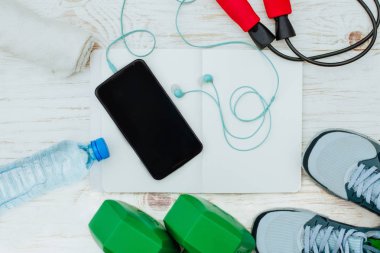 Fitness, sağlıklı ve aktif yaşam kavramı, ip atlama, halter, spor ayakkabı, şişe suyu, beyaz arka plan üzerinde kulaklık ile akıllı telefon. Üstten Görünüm