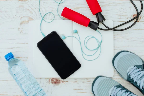 Fitness, sağlıklı ve aktif yaşam kavramı, ip atlama, spor ayakkabı, şişe suyu, beyaz arka plan üzerinde kulaklık ile akıllı telefon. Üstten Görünüm