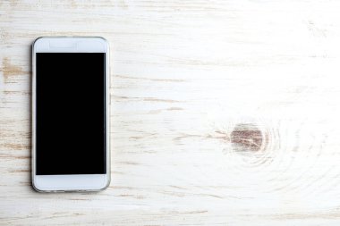  Beyaz ahşap zemin üzerinde beyaz cep telefonu. Kopya alanı, üstten görünüm