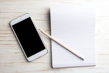 Not defteri ve kalem ile beyaz ahşap arka plan üstünde hareket eden telefon