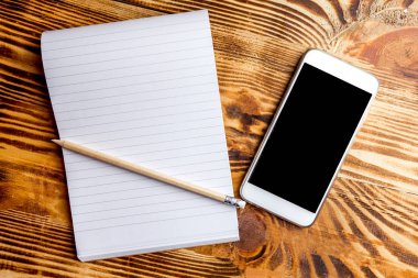 Not defteri ve kalem ile koyu ahşap arka plan üstünde hareket eden telefon