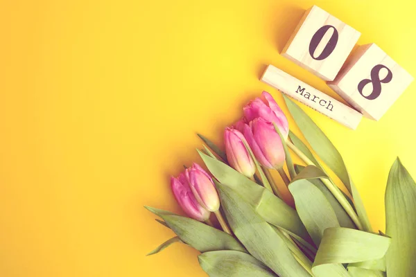 8 March Happy Women\'s Day concept. With wooden block calendar and pink tulips on yellow background. Copy space