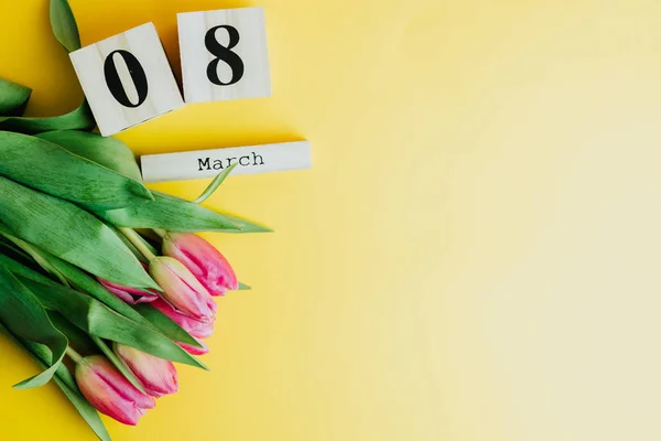 8 March Happy Women\'s Day concept. With wooden block calendar and pink tulips on yellow background. Copy space