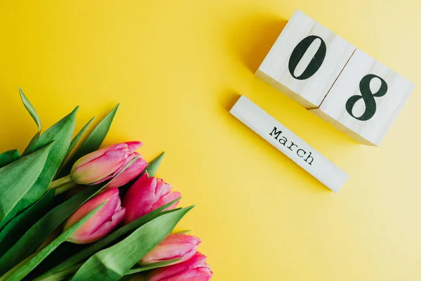 8 March Happy Women\'s Day concept. With wooden block calendar and pink tulips on yellow background. Copy space