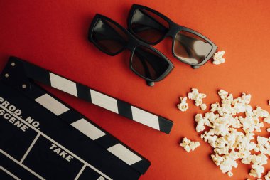 Sinema en az kavramı. Sinemada film izlemek. Clapper masa, 3d gözlük, kırmızı bir arka plan üzerinde patlamış mısır. 