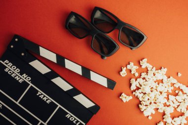 Sinema en az kavramı. Sinemada film izlemek. Clapper masa, 3d gözlük, kırmızı bir arka plan üzerinde patlamış mısır. 