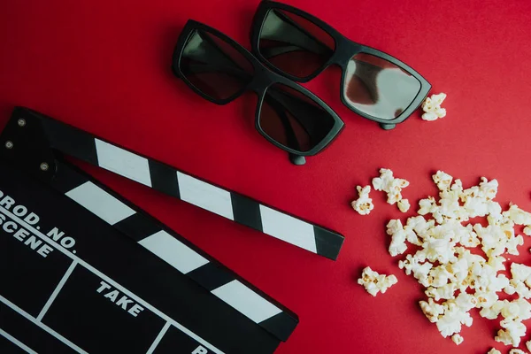 Sinema en az kavramı. Sinemada film izlemek. Clapper masa, 3d gözlük, kırmızı bir arka plan üzerinde patlamış mısır. 
