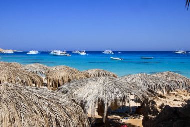 Deniz manzarası ile hasır şemsiyeler ve yatlar.