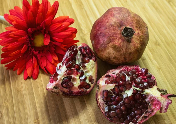 Still life with pomegranate and flower on the wooden background. A whole and cut pomegranate.