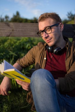 Mavi gökyüzü arka plan üzerinde kitap okuma gözlük bir adam portresi.