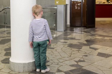 2019.05.10, Tula, Rusya. Beyaz bir sütunun yanında duran çizgili hırka giyen küçük bir çocuk. Çocuk, anne ve babasından rahatsız oldu..