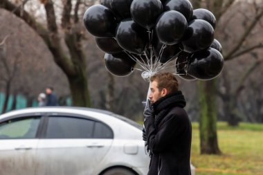 2015.11.22, Moskova, Rusya. Doğum günü hüzünlü bir tatil konseptidir. Siyah atkı ve ceket giyen genç sarışın bir adam elinde siyah balonlar ve sigara içen bir adam..