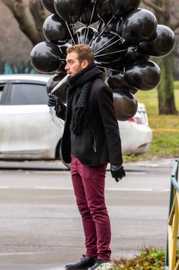 2015.11.22, Moskova, Rusya. Doğum günü hüzünlü bir tatil konseptidir. Siyah atkı ve ceket giyen genç sarışın bir adam elinde siyah balonlar ve sigara içen bir adam..