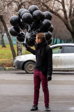 2015.11.22, Moskova, Rusya. Doğum günü hüzünlü bir tatil konseptidir. Siyah atkı ve ceket giyen genç sarışın bir adam elinde siyah balonlar ve sigara içen bir adam..