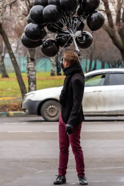 2015.11.22, Moskova, Rusya. Doğum günü hüzünlü bir tatil konseptidir. Siyah atkı ve ceket giyen genç sarışın bir adam elinde siyah balonlar ve sigara içen bir adam..