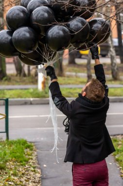 2015.11.22, Moskova, Rusya. Doğum günü hüzünlü bir tatil konseptidir. Siyah atkı ve palto giyen genç sarışın bir adam ağaç dallarına dolanmış düzinelerce balon bırakıyor..