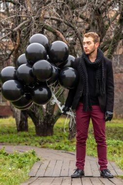 2015.11.22, Moskova, Rusya. Doğum günü hüzünlü bir tatil konseptidir. Siyah atkı ve ceket giyen genç sarışın bir adam elinde siyah balonlar ve başka yöne bakıyor..