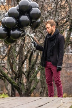 2015.11.22, Moskova, Rusya. Doğum günü hüzünlü bir tatil konseptidir. Siyah atkı ve ceket giyen genç sarışın bir adam elinde siyah balonlar ve başka yöne bakıyor..
